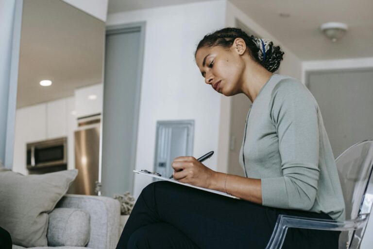 Concentrated ethnic female interviewer or psychotherapist taking notes in clipboard